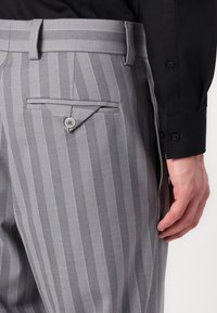 Grey striped trousers with a buttoned back pocket, made of a smooth fabric. Includes belt loops and a tailored fit.
