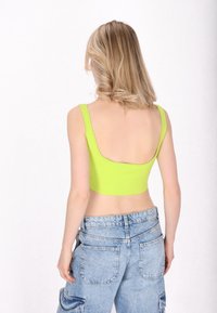 Heldere limoen groene crop-top met brede schouderbanden en een lage rug, gecombineerd met hooggerande lichtblauwe denim cargo-broek.