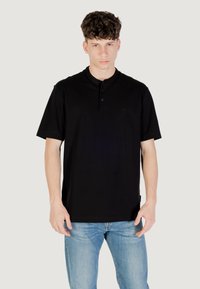 Camisa polo negra de manga corta con tapeta de botones, fabricada en tejido suave. Presenta un pequeño logotipo en el pecho y un corte relajado.