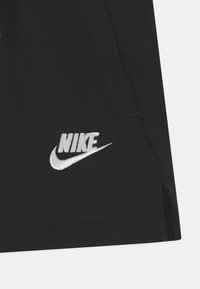Čierne atletické šortky vyrobené z bavlnenej zmesi, s bielou vyšívanou Nike logom na dolnej ľavej strane a bočnými švovými vreckami.