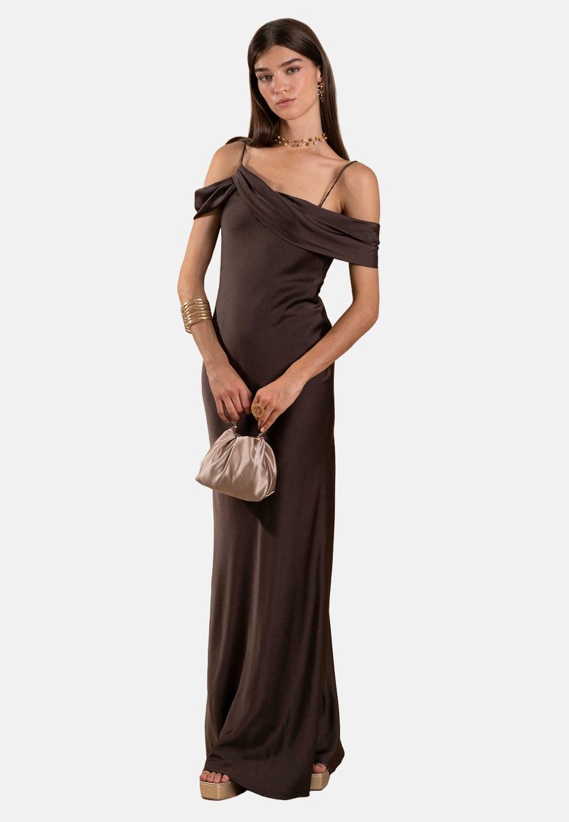 Braunes Abendkleid mit schulterfreiem Design, figurbetontem Schnitt und weicher Textur. Das Model hält eine kleine, taupefarbene Satin-Handtasche.