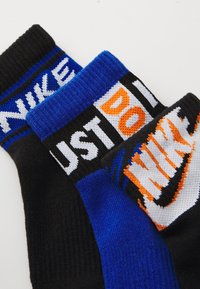 Három pár Nike zokni: egy fekete fehér logóval, egy kék "JUST DO IT" felirattal fekete és narancssárga színben, és egy fekete narancssárga logóval.