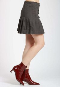 Gonna grigia plissettata con vita alta e dettagli con bottoni, abbinata a stivaletti rossi lucidi con punte affilate e tacchi spessi.