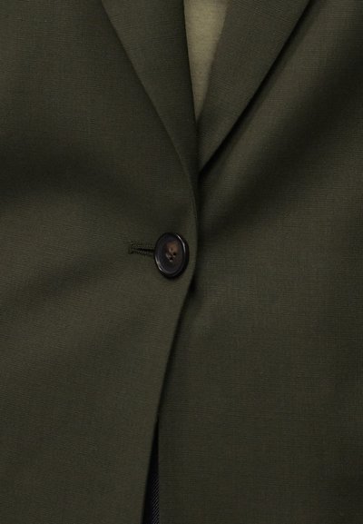 Μονό μαύρο κουμπί ραμμένο σε σκούρο ελιάς πράσινο σακάκι με κόψιμο γιακά, που δείχνει λεία υφή υφάσματος και ελαφριές ζάρες.