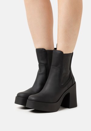 Bottes noires en cuir, montantes jusqu'à la cheville, avec une plateforme épaisse et un talon carré. Elles présentent des panneaux latéraux élastiques et des détails de couture, avec une finition texturée.