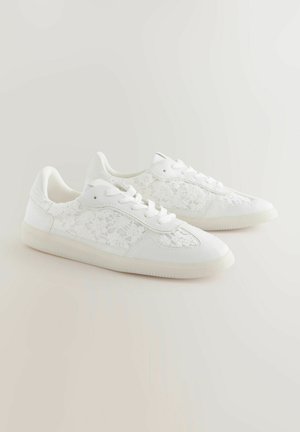 Hvide sneakers med snøredetaljer på siderne, tekstureret mønster, rund tå, flad gummisål og forstærket hæl og tunge.
