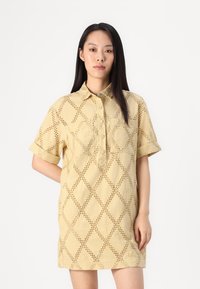 Abito camicia a manica corta di colore giallo chiaro, con un motivo a rombi ritagliato, chiusura con bottoni e una vestibilità comoda. Realizzato in tessuto testurizzato.