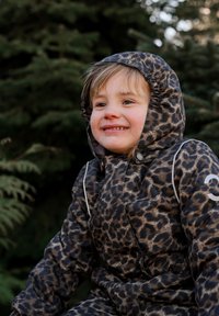 Leopardenmuster-Steppjacke mit Kapuze, in Schwarz- und Brauntönen, mit elastischen Bündchen und silbernen Akzenten, getragen von einem Kind im Freien.