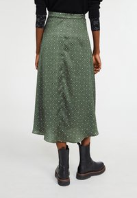 Grøn midi-nederdel med blomstermønster, blødt stof, glat tekstur og en udvidet silhuet. Kombineret med sorte ankelstøvler.