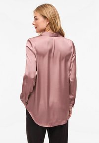 Gari piedurkņu, viegli mauves krāsas satīna krekls ar apaļu apakšu, redzamām plecu šuvēm un ar pogām aizpogātiem aprocēm. Gluda tekstūra; minimālas detaļas.