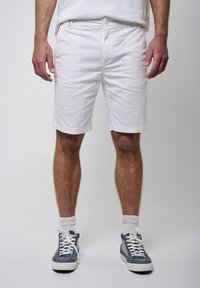 Bermudas de algodón blancas con corte recto, bolsillos delanteros y cierre de botón. Se llevan con zapatillas grises y calcetines blancos. Diseño sencillo, sin patrones.