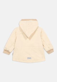 Ανοιχτό μπεζ μπουφάν με κουκούλα, ριμπ μανσέτες και ίσια γραμμή. Διαθέτει μικρή ετικέτα με το λογότυπο της μάρκας στο πίσω μέρος. Λείο υλικό και μίνιμαλ σχεδιασμός.