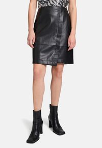 Schwarzer Lederwickelrock mit einer glatten Textur und maßgeschneidertem Schnitt. Kombiniert mit schwarzen Knöchelboots mit quadrater Zehenform und Blockabsatz.