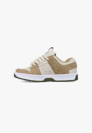 Beige-weißer Sneaker mit niedrigem Schnitt, Veloursleder-Details, weißen Schnürsenkeln und grünen Akzenten an Sohle und Fersenlasche, von der Außenseite gezeigt.