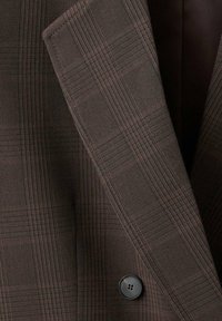 Blazer marrone con motivo a quadri, realizzato in tessuto strutturato, con chiusura a un bottone nero. Primo piano del colletto e della revers.