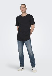 Schwarzes T-Shirt mit kurzen Ärmeln, Rundhalsausschnitt, lockerer Passform; getragen mit blauer Jeans und weißen Sneakers, mit einem schlichten Design.