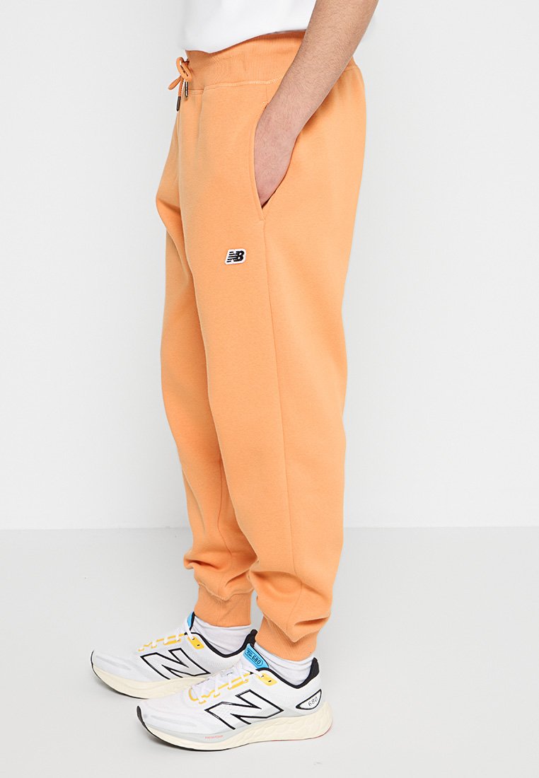 Pantalones de chándal naranja con cinturilla elástica y cordón, que cuentan con bolsillos laterales y un pequeño logo de New Balance. Material suave de mezcla de algodón.