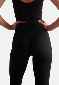 Black ribbed leggings with a high waist and minimal branding. The fabric features a textured pattern and snug fit for comfort.