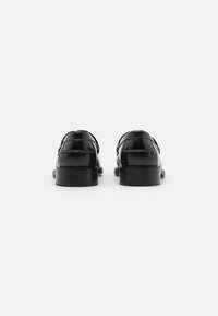 Zwarte leren schoenen met een gladde afwerking, ronde neus en dubbele gespdetails; lage, platte hakken zorgen voor een klassieke silhouet.