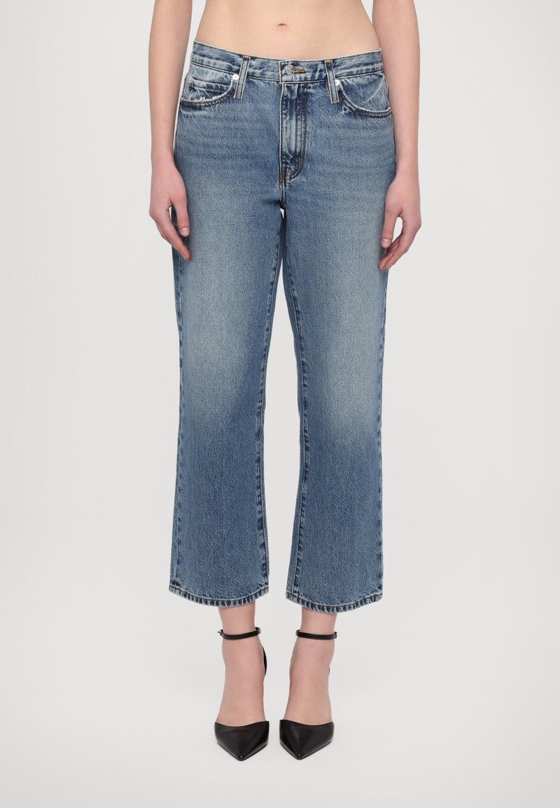 Lyseblå denimjeans med høyt liv, rett skjne, flagrende nederkant og to frontlommer. Brukt med svarte spisse hæler.