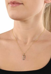 Collar de cadena dorada con un colgante ovalado que presenta una superficie texturizada, exhibido sobre piel desnuda y una blusa negra.