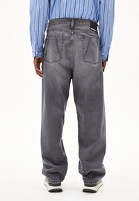 Zwarte denim jeans met dubbele achterzakken, elastische tailleband en zichtbare stiksels. Draag met een blauw gestreept shirt en sneakers.