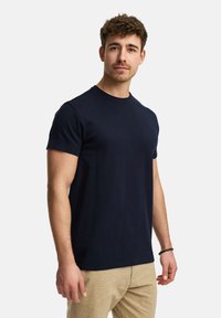 Navy blue' bawełniana koszulka z krótkim rękawem i okrągłym dekoltem, prezentowana na męskim modelu, o gładkim wzorze i regularnym kroju.