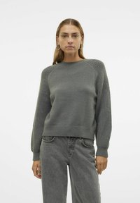 Maglione grigio a maglia con maniche raglan e dettagli a coste sul colletto e sull'orlo, abbinato a jeans grigi a vita alta.