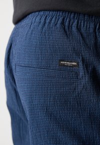 Navyblauwe textuurschorting met een elastische tailleband en een achterzak met een zwart label met de tekst "SCOTCH & SODA."