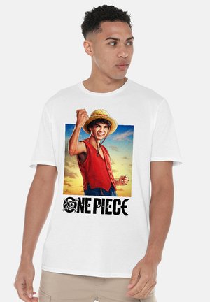 Young man wearing white t-shirt with colorful One Piece character raising fist and text below, standing against plain background.