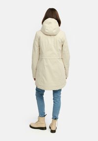 Ljusbeige jacka med huva, åtsittande midja och två sidofickor, tillsammans med ljusblå jeans och beige snörstövlar.