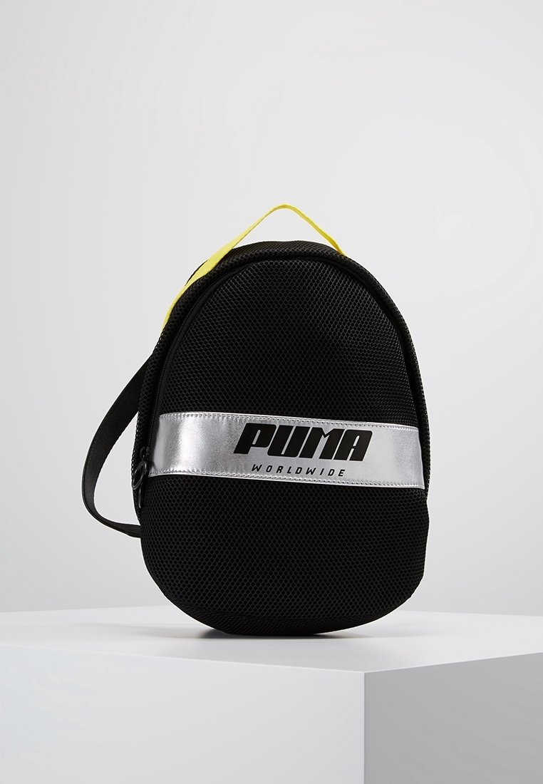 Mochila de malla negra con asa amarilla, logo plateado de PUMA y correa ajustable. Forma circular con superficie texturizada y detalles de costura visibles.