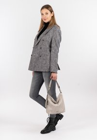 Grå dobbeltbrystet blazer med et struktureret mønster, parret med slanke grå jeans og sorte snørebåndsstøvler. Modellen holder en lysegrå håndtaske.