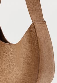 Τσαντάκι ώμου από ταμπά δέρμα με υφή, ευρύ λουράκι και μίνιμαλ σχεδιασμό, με λεπτές ραφές και ανάγλυφο όνομα επωνυμίας.