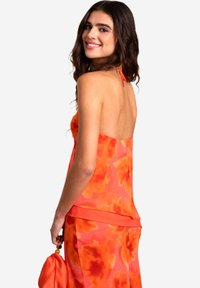 Orange-blumengemustertes Haltertop-Kleid mit lockerer Passform, fließender Textur und einer passenden Tasche in der Hand.