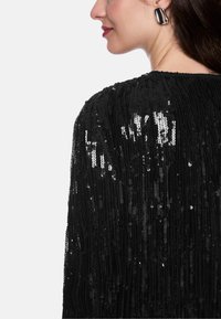 Black sequined top featuring a textured design with vertical stripes. Notable shiny accents and a round neckline complete the look.