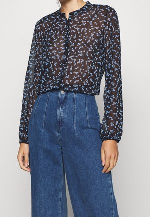 Sheer black blouse with blue floral pattern paired with high-waisted, wide-leg blue denim jeans on a standing person.
