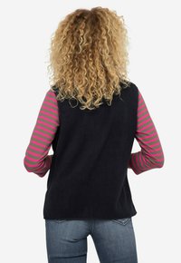 Czarna kamizelka z polaru, z długimi rękawami w szare i różowe paski, charakteryzująca się miękką teksturą i luźnym krojem, noszona z niebieskimi dżinsami.