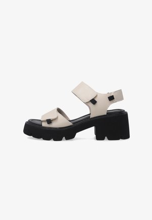 Beige open-toe sandal with thick black chunky sole, adjustable straps over toes and ankle, and sturdy block heel for support.
