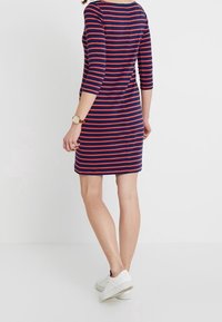 Navy blue dressi punaisilla vaakaraitoja, kolmeen neljännekseen hihat, pyöreä kaula-aukko, yhdistettynä valkoisiin tennareihin ja kelloon.