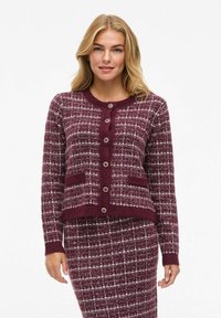 Cardigan en tricot bordeaux avec un motif à carreaux, un col rond, une fermeture à boutons et des poches avant, associé à une jupe assortie.