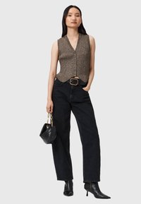 Dzianinowe kamizelki w złotobrązowym kolorze, z dekoltem w serek, dopasowanym krojem i z przodem zapinanym na guziki; w połączeniu z czarnymi dżinsami o wysokim stanie i czarnymi akcesoriami.