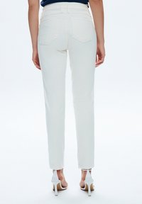 Pantalones blancos de cintura alta con bolsillos traseros, ajustados y de textura suave. Combinados con sandalias blancas de tacón alto.