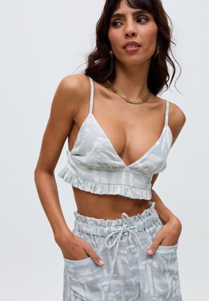 Woman wearing light blue patterned crop top with ruffle hem and matching drawstring shorts, posing with hands in pockets.