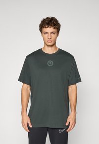 Mørkegrøn bomulds t-shirt med rund halsudskæring, korte ærmer og et rundt logo på brystet; glat tekstur, afslappet pasform.