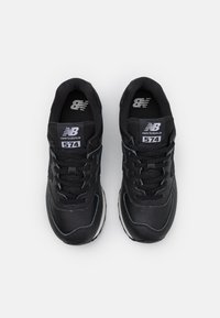 Paire de baskets noires New Balance 574 avec des lacets noirs et des écussons blancs de logo sur les languettes, vues de dessus sur fond blanc.