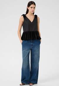 Haut peplum noir avec décolleté en V, en tissu satiné au niveau du bodice et volant en velours. Associé à un jean en denim bleu à jambes larges.