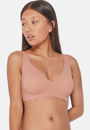 Sostén inalámbrico en un suave material de color rosa claro. Presenta un escote en V profundo y tirantes anchos, diseñado para comodidad y soporte.