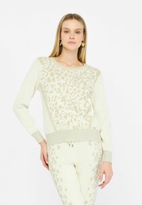 Maglione lavorato a maglia beige con design a motivo leopardo in una tonalità più chiara, con polsini a coste e scollatura rotonda. Presenti dettagli testurizzati.