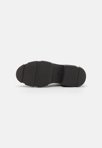 Semelle de chaussure noire présentant un design texturé et segmenté avec trois rainures proéminentes et une pointe arrondie, fabriquée en matériau en caoutchouc durable.